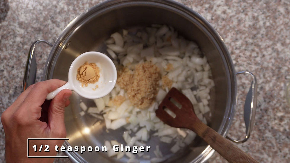 Hand adds 1/2 tsp ginger into a pot with chopped onions, next to a wooden spatula on a speckled countertop.