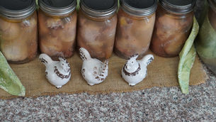Ceramic chickens in front of mason jars with canned food on burlap, flanked by green patterned napkins. Cozy, rustic kitchen vibe.