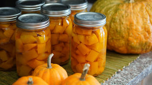 Jars of diced orange pumpkins on a table, surrounded by small whole pumpkins, creating an autumn harvest vibe.