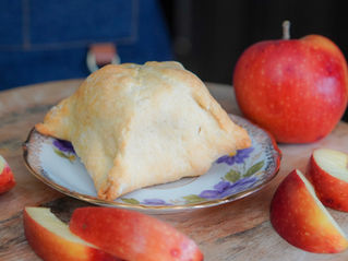 Apple hand pie on a floral plate, surrounded by red apple slices and a whole apple on a wooden board.