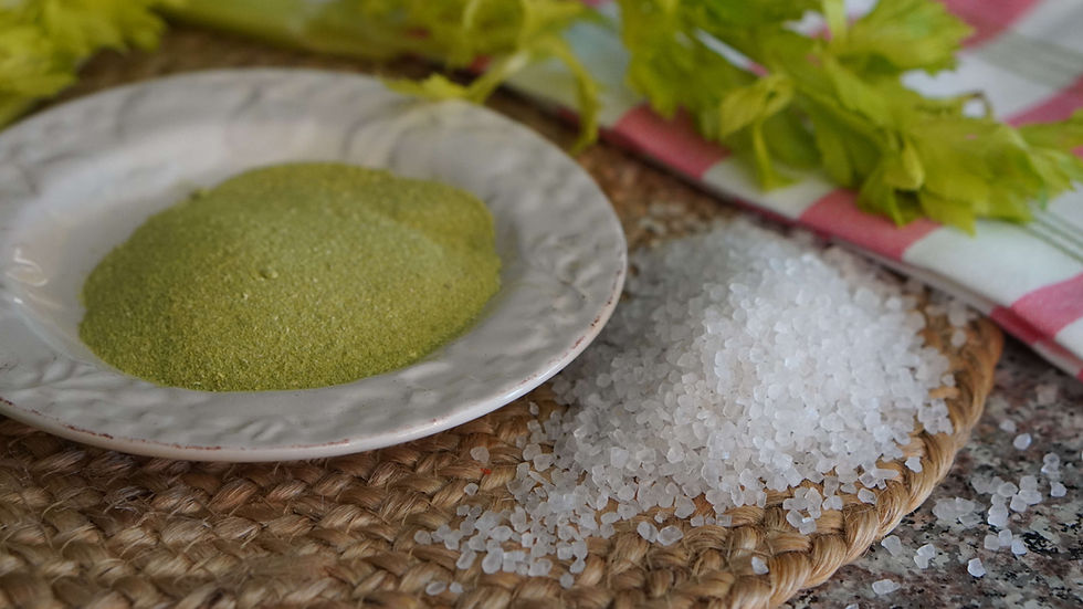 Green powder on a plate and coarse salt on a woven mat, with fresh celery and a striped cloth in the background. Rustic kitchen setting.