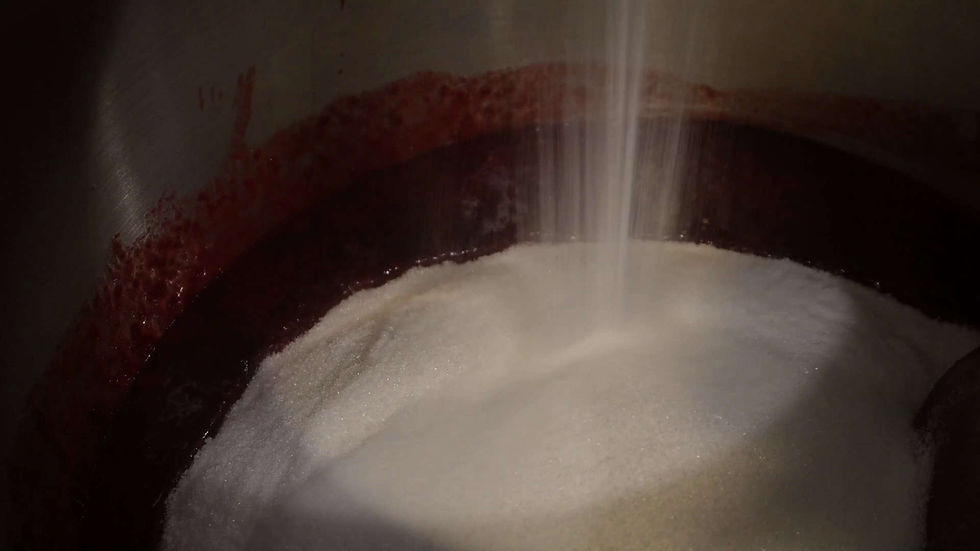 Sugar falling into a metal mixing bowl with red liquid residues on the side. Light highlights the sugar, creating a dynamic motion effect.