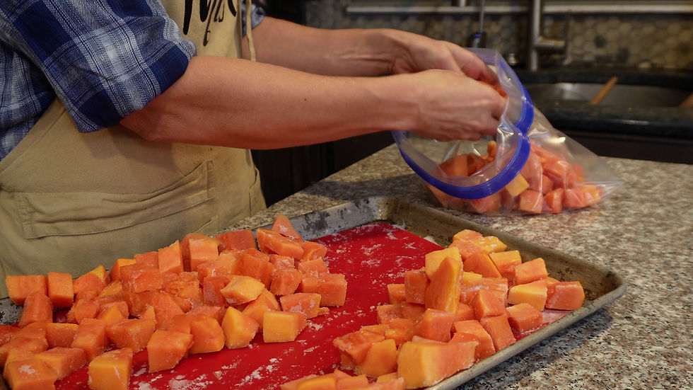 A person in a blue plaid shirt and apron places diced orange fruit into a ziplock bag on a granite countertop with red liner.