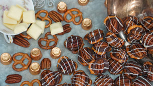 Pretzels, pecans, and chocolates with white drizzle on a tray, alongside white chocolate squares, creating a festive, appetizing display.