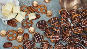 Pretzels, pecans, and chocolates with white drizzle on a tray, alongside white chocolate squares, creating a festive, appetizing display.