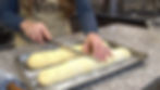 Hands cut dough on a floured tray in a kitchen. Granite countertop, apron with "Maria" text. Knife and rolling pin visible.