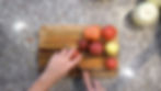 Hands slice a tomato on a wooden cutting board with assorted tomatoes. Gray countertop background, preparing ingredients, top view.