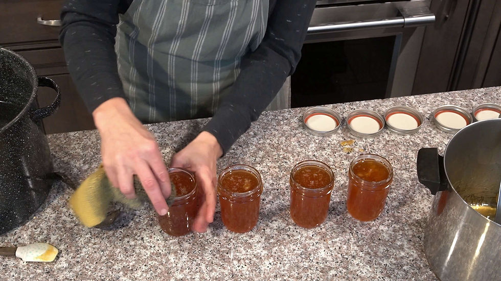 Person in striped apron sealing jars of orange preserve on a granite countertop, with lids and a large pot nearby. Cozy kitchen setting.