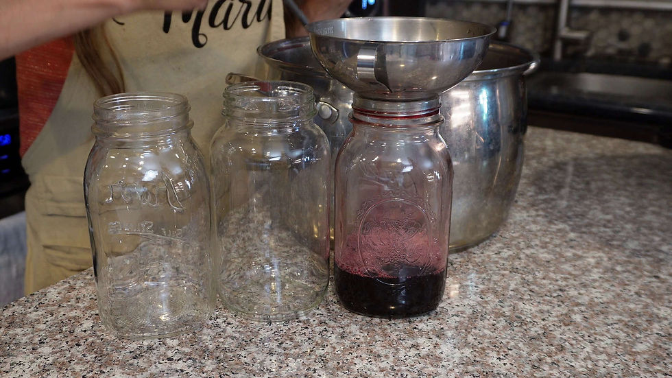 Three glass jars on a granite countertop; one filled with purple liquid under a metal funnel. Background shows a kitchen setting.