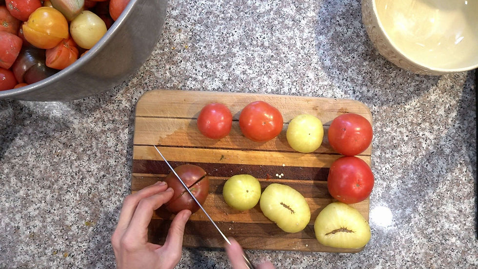 Hands slice red tomato on a wooden board with yellow and red tomatoes. A bowl of mixed tomatoes sits nearby on a speckled countertop.