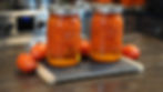 Two jars of canned tomatoes on a wooden board, surrounded by fresh tomatoes in a kitchen setting. Warm, rustic atmosphere.