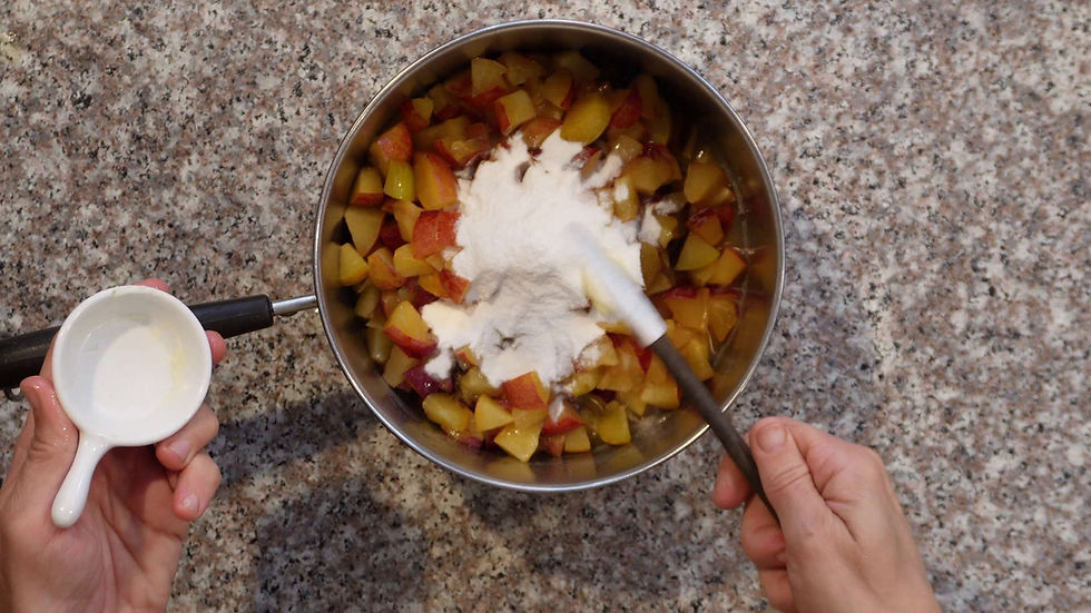 Hands stirring diced fruit and flour in a pot on a speckled countertop; an empty measuring cup is held on the side.