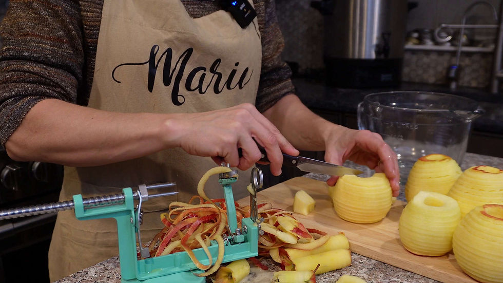 Person peeling apples on a kitchen counter with a teal peeler. They're wearing an apron labeled "Mari." Peeled apples on a cutting board.