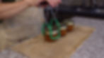 Hands use jar lifter to move three jars on burlap mat in a kitchen. The jars have metal lids and are filled with orange contents.