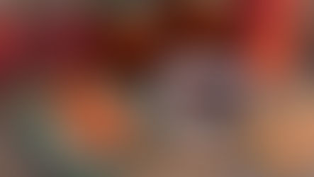 Peaches, jam jars, and bread on a woven mat. Slices with peach jam on a green plate. A white dish with a spoon holds more jam nearby.