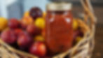 A beautiful jar of canned plum chutney in a basket full of plums.