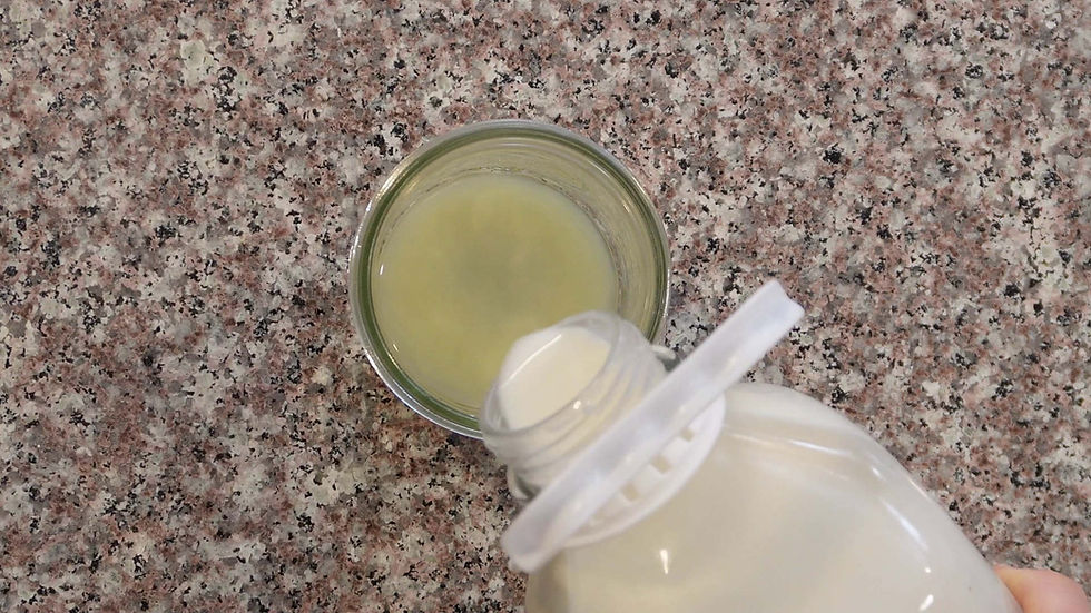 Pouring white liquid from a bottle into a glass of yellow liquid, on a speckled countertop. Top view, close-up.