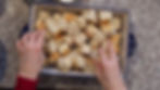 Hands arranging bread cubes in a decorative dish on a speckled countertop. The dish has a blue floral pattern.