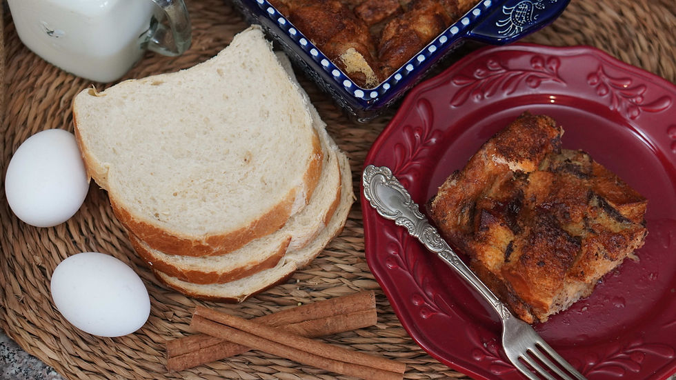 Bread slices, two eggs, and cinnamon sticks on a woven mat, next to bread pudding on a red plate with a fork. Background shows a milk jug.