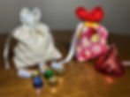 Two decorated fabric bags with bunny ears, one floral and the other with ladybugs, are on a table with wrapped chocolates.