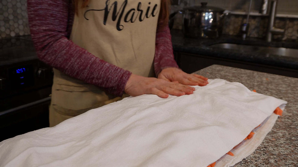 Hands pressing a white cloth on a countertop, wearing an apron with the name "Marie." Kitchen setting with subtle lighting and warm tones.