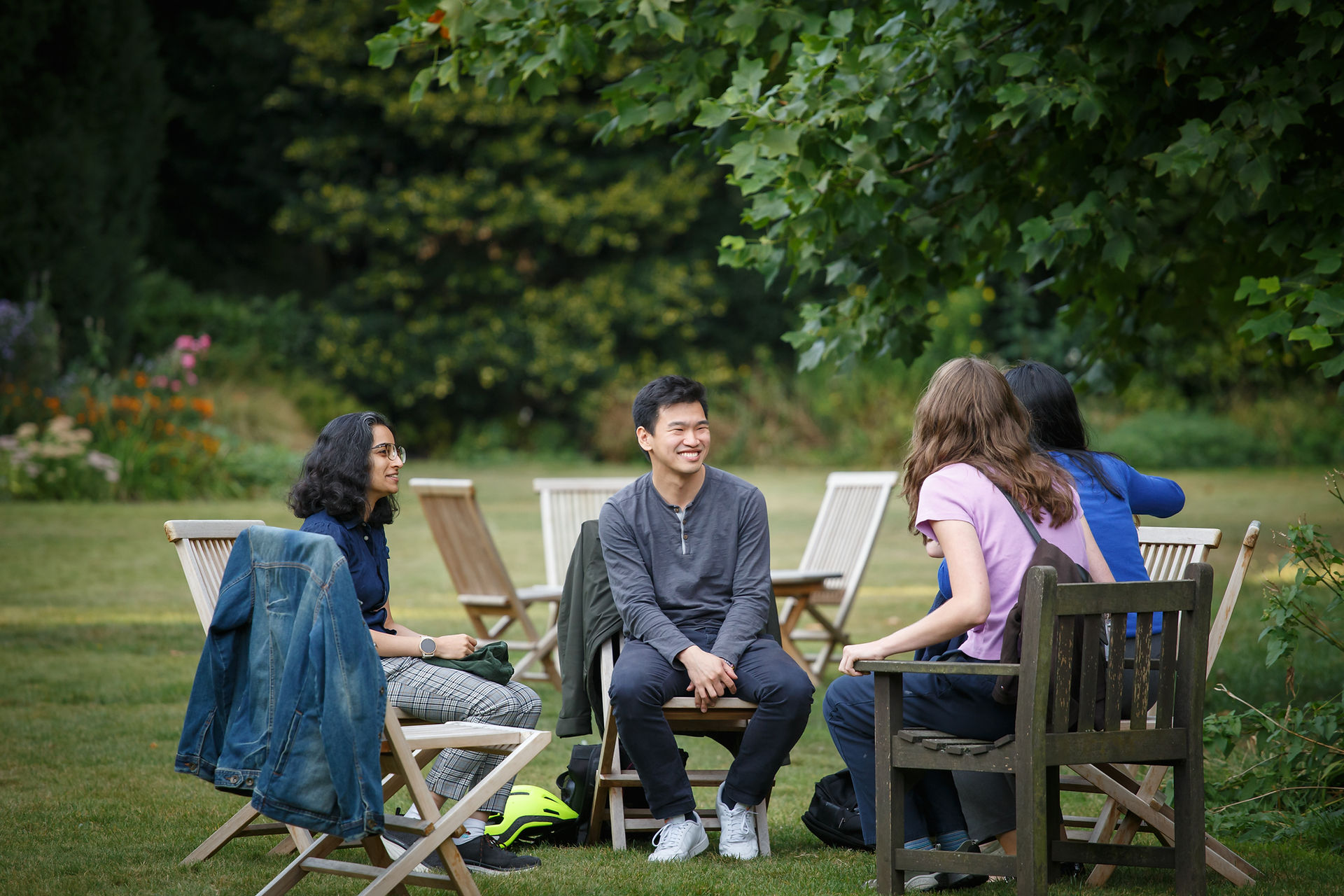Students in college garden chatting whilst seated on wooden garden furniture