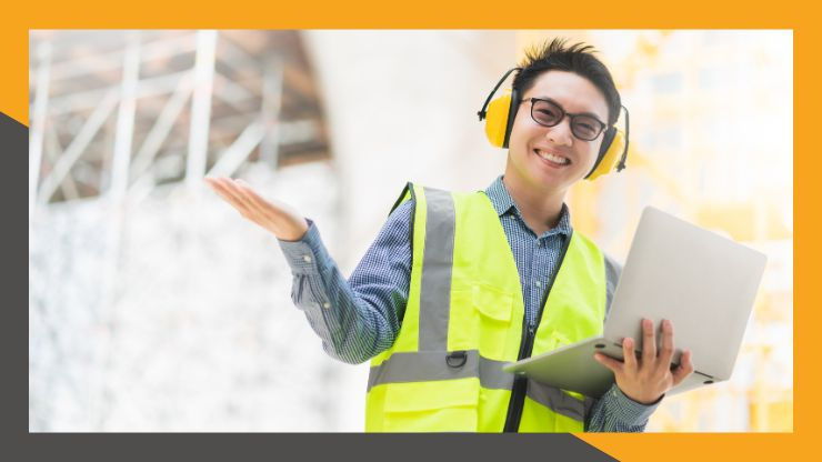 Smiling person in safety gear with yellow vest and headphones, holding a laptop. Bright construction site background with metal scaffolding.