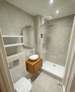 Refurbished bathroom with raised shower, wooden vanity, and back-to-wall toilet in Islington N1 3EU