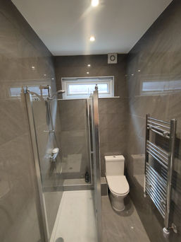 Modern bathroom with glossy grey tiles, towel radiator, and walk-in shower in Harrow