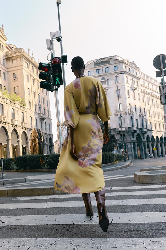 Uma modelo negra com um vestido amarelo florido posando na rua