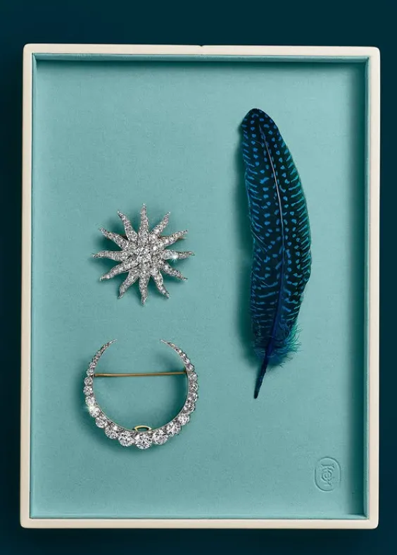 broche de luna, broche de sol y pluma azul oscuro sobre fondo azul