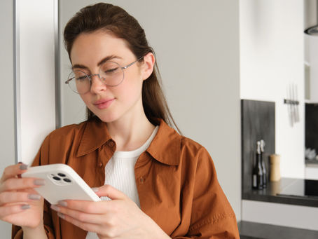 chica con gafas, top blanco y camisa marrón viendo el móvil en la cocina