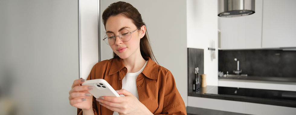 chica con gafas, top blanco y camisa marrón viendo el móvil en la cocina