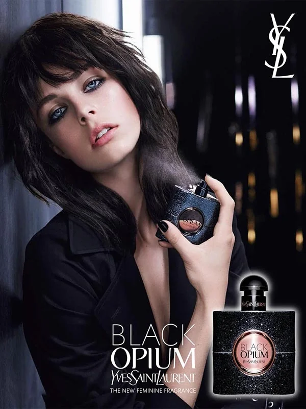 mujer con flequillo y pelo oscuro lleva una camisa negra y sujeta un perfume