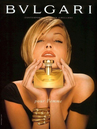 mujer rubia con vestido negro sujeta un perfume cerca de su cara con las dos manos