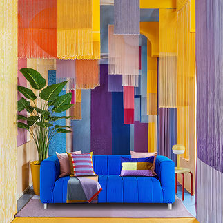 habitación donde se ve un sofá azul con cojines de colores, una planta a la izquierda, una mesa con una lamparita a la derecha y del techo cuelgan telas con flecos