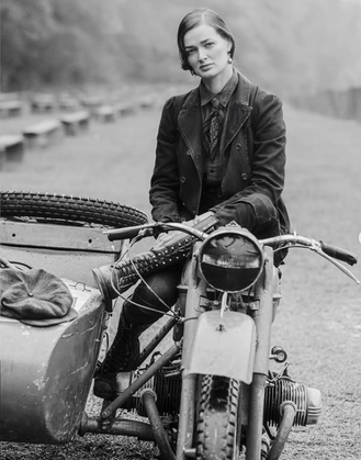 Chica subida a una moto y vestida con camisa, chaqueta y botas