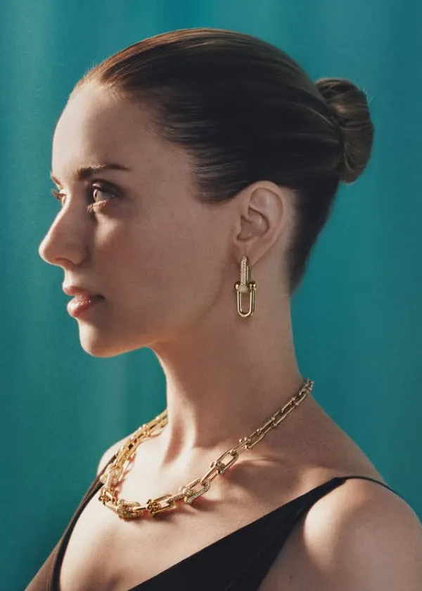 chica de perfil con un moño, vestido negro , collar dorado y pendientes dorados 