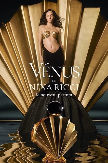 mujer con vestido negro y dorado posa junto a una concha dorada gigante