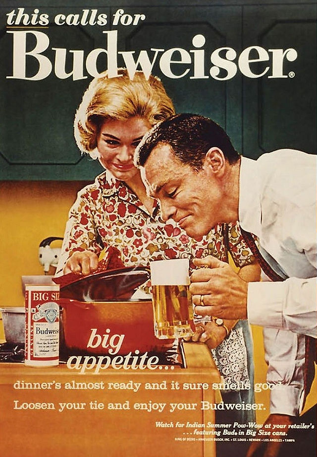 Anuncio de cerveza Budweiser. Mujer enseñando a un hombre lo que ha cocinado mientras que el hombre está atento a la cerveza 