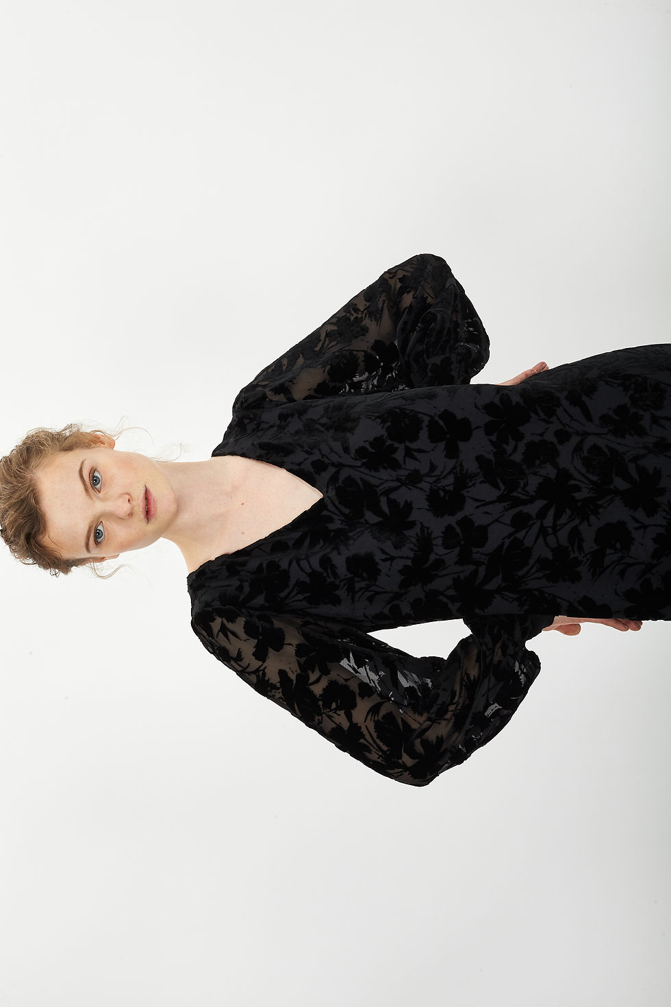 Chica rubia con el pelo rubio y ojos claros lleva un vestido negro con estampado de flores del mismo color