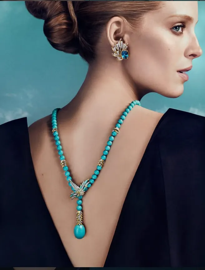 mujer de espaldas vestida de oscuro y con el pelo recogido lleva unos pendientes dorados y un collar azul