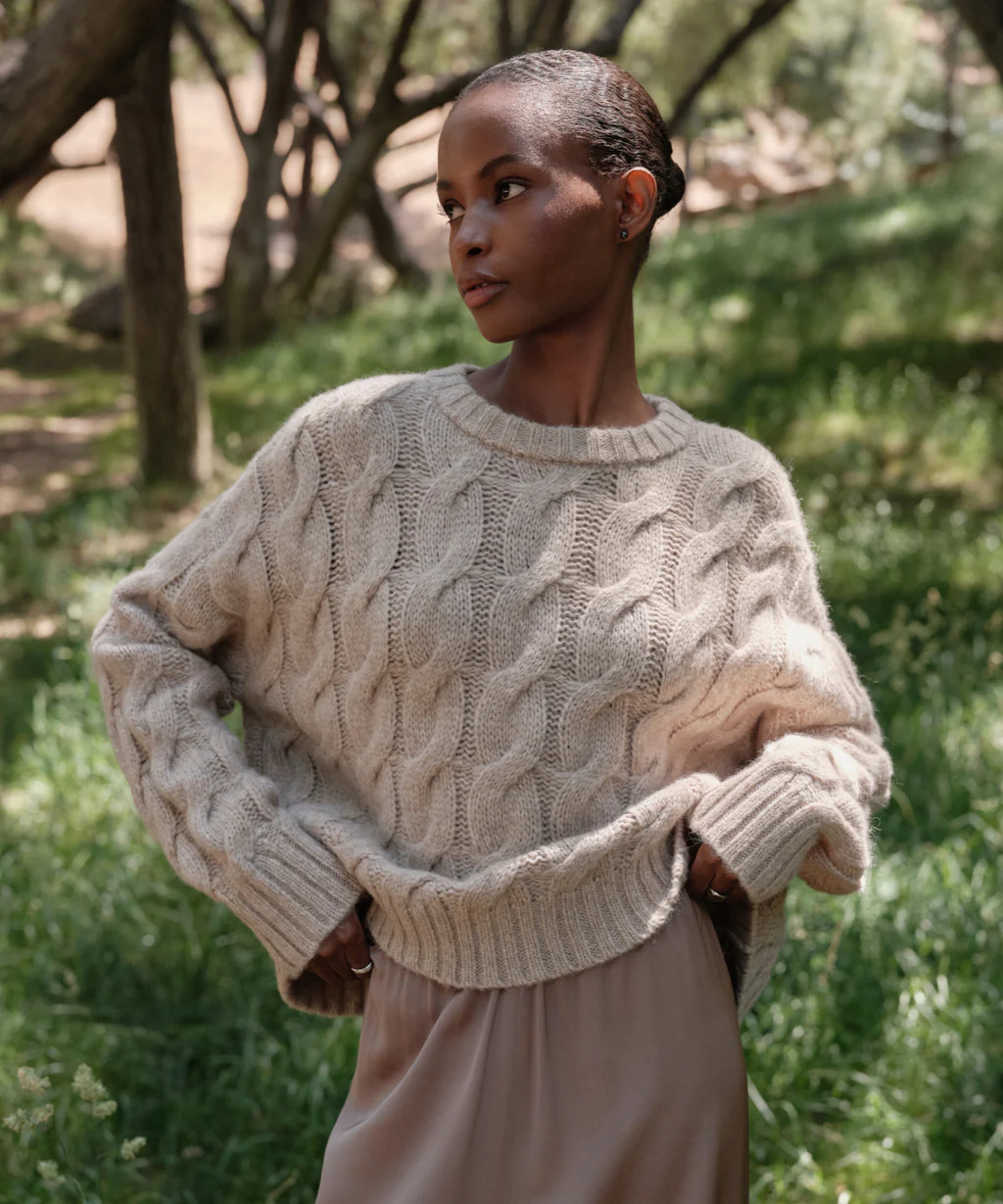 Woman in a forest wearing a beige sweater and beige pants