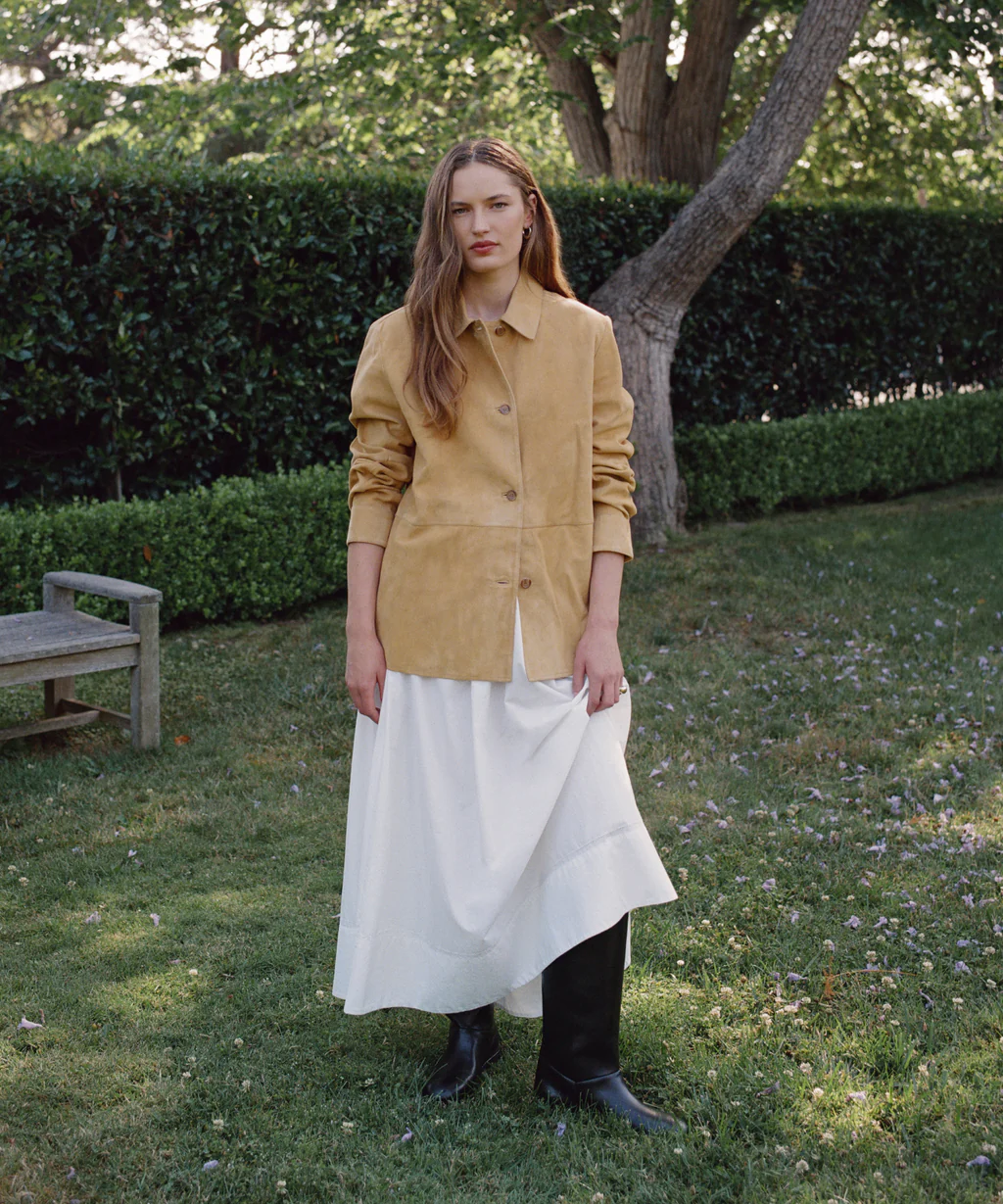 Woman in a garden wearing a yellow shirt, a long white skirt, and black boots