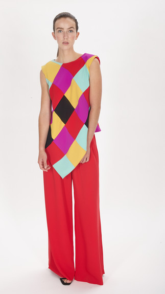 Moça vestida com uma calça longa e larga vermelha e uma blusa sem mangas com losangos de várias cores.