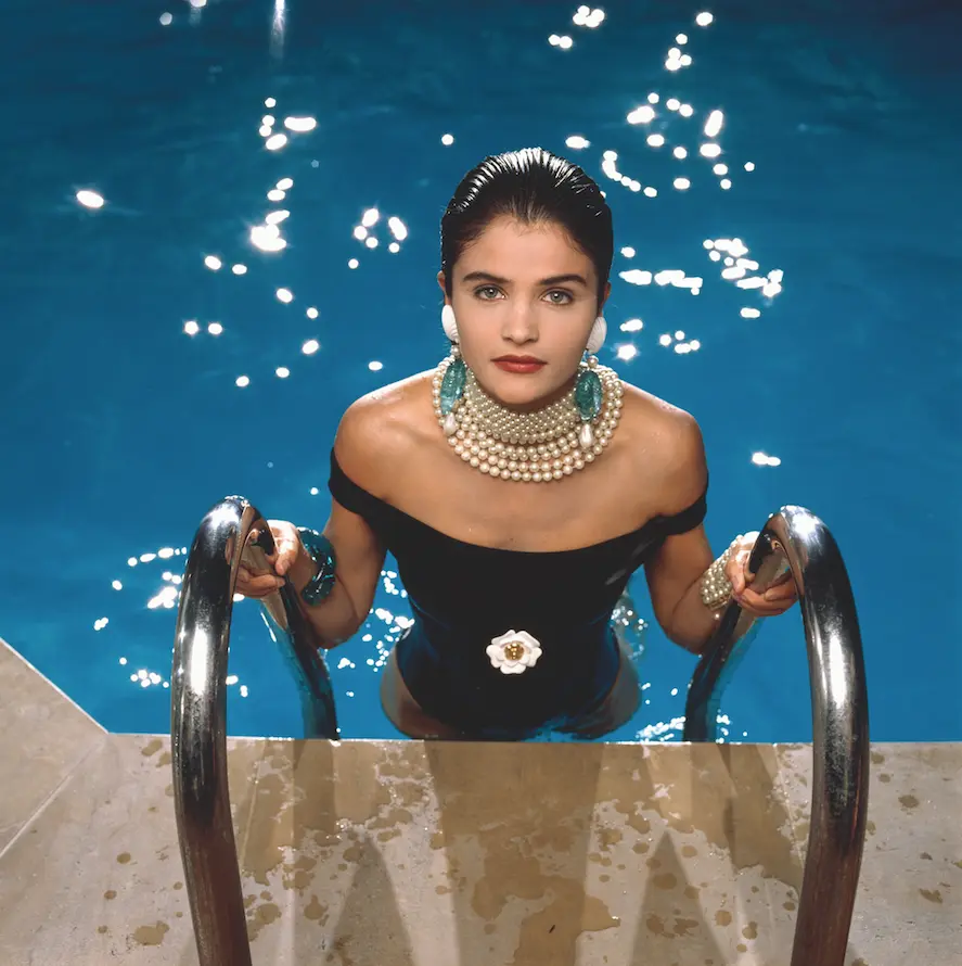 chica con el pelo recogido, bañador negro y accesorios de perlas saliendo de la piscina.