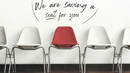Four white chairs with one red one in the middle with the text above it that reads "We are saving a seat for you!"