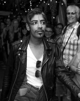 King Mandita in a black leather jacket, painted moustache and sunglasses tucked into his shirt