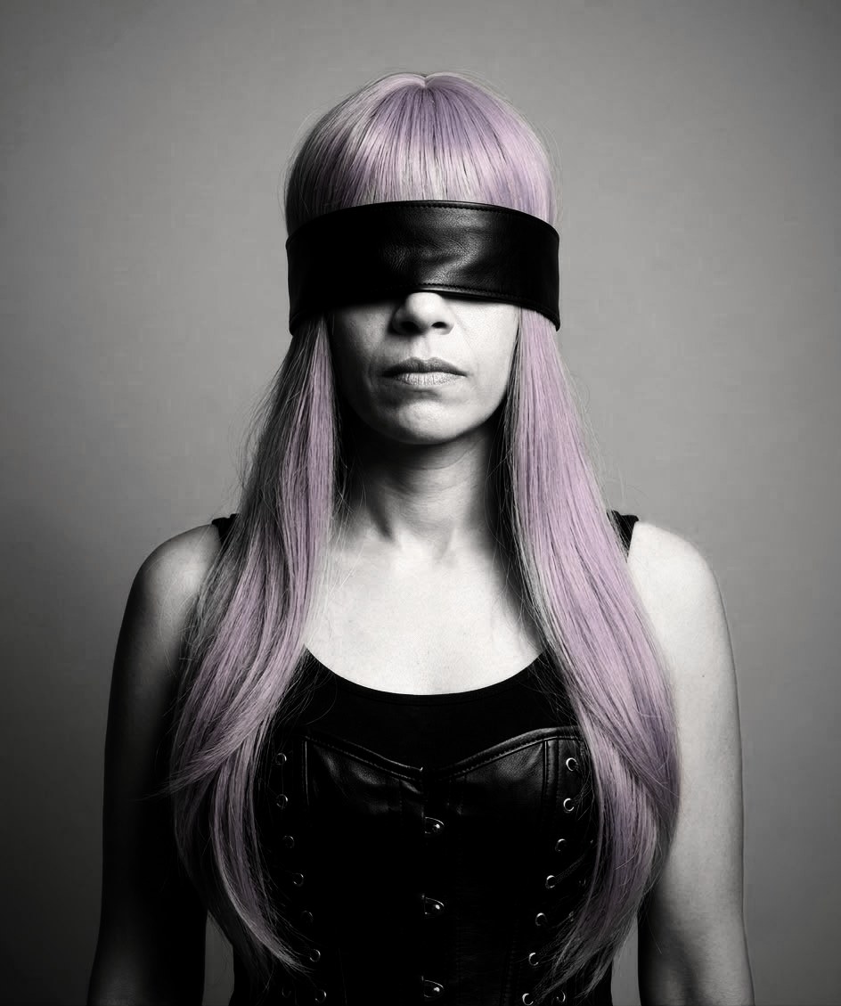 Black-and-white portrait of O, blindfolded in black leather, with a lilac wig