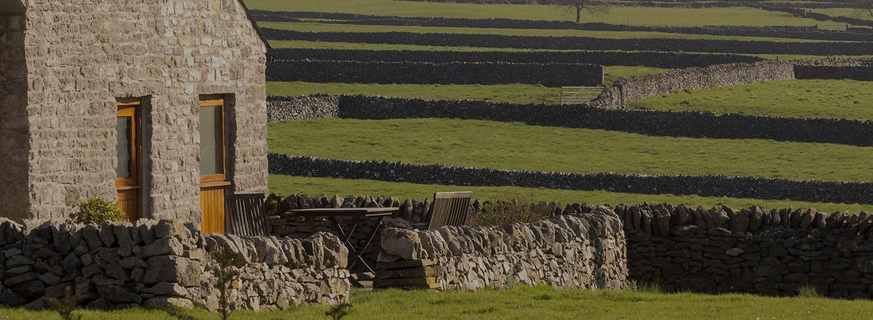 A house in the countryside surrounded by fields and drystone walls.